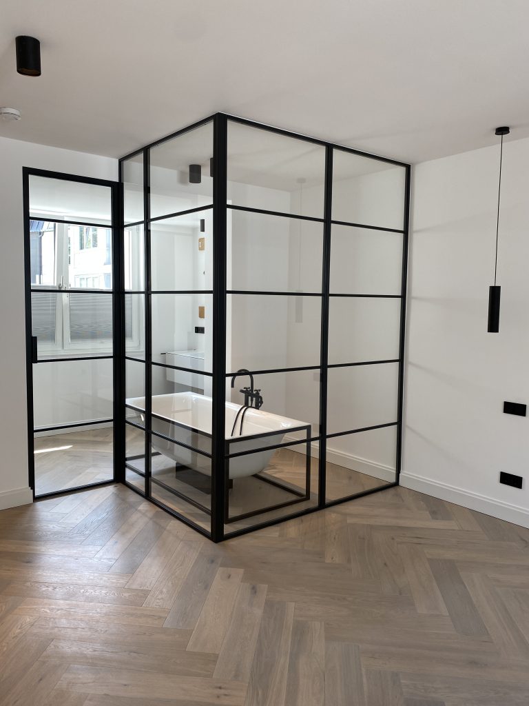 Lofttür und Glaswand als Trennwand zwischen Schlafzimmer und Bad