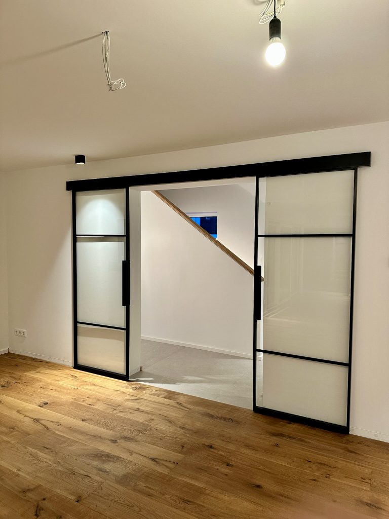 Doppelte Loft-Schiebetür mit Klarglas zwischen Wohnraum und Treppenhaus