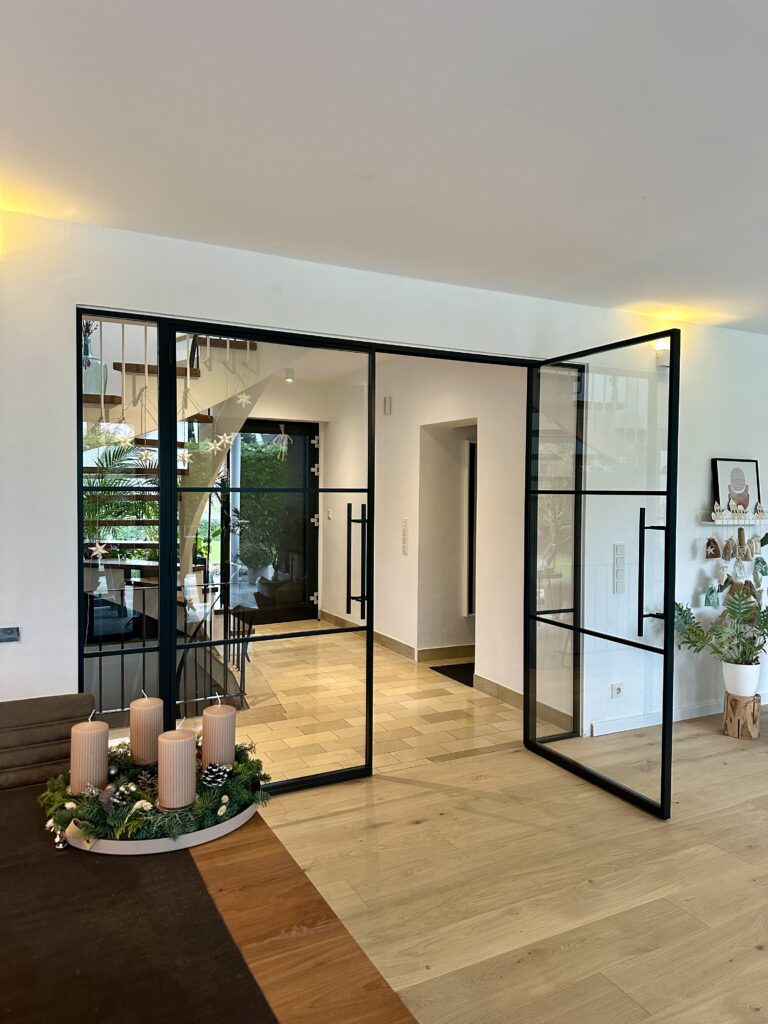 Doppelflügelige Lofttür als Raumteiler zwischen Treppenhaus und Wohnzimmer aus schwarzem Stahl RAL 9005 mit Klarglas