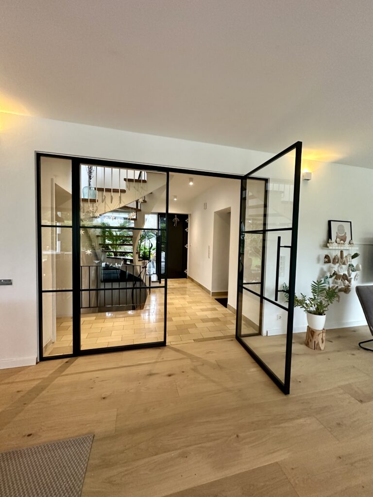 Doppelflügelige Lofttür als Raumteiler zwischen Treppenhaus und Wohnzimmer aus schwarzem Stahl RAL 9005 mit Klarglas