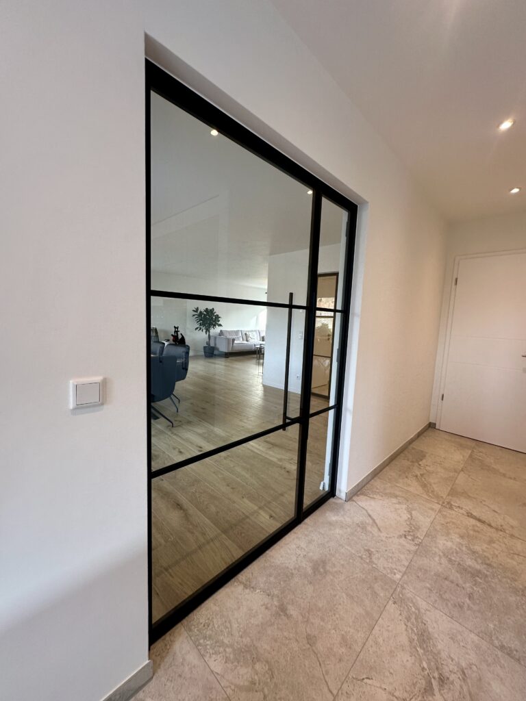 Lofttür Drehflügeltür mit fixem Seitenteil aus schwarzem Stahl und Klarglas im Wohnzimmer